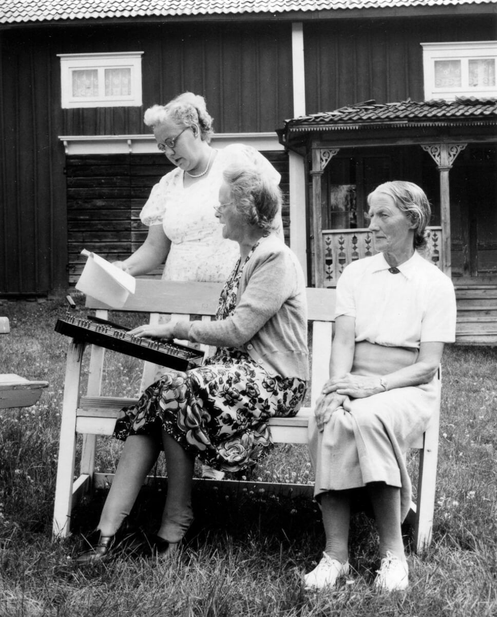 Tre kvinnor vid bänk på gårdsplan som spelar och sjunger.