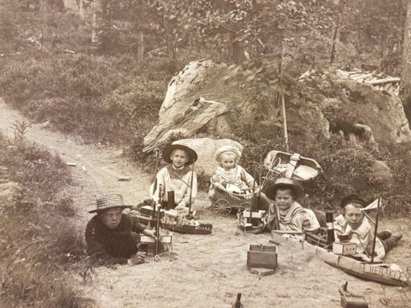 Fem barn sitter med leksaksbåtar i skogen.