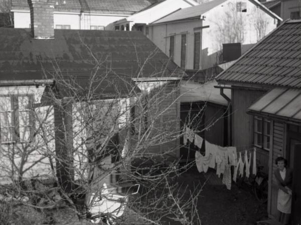 En stadsinnergård med upphängd tvätt på en tvättlina samt en kvinna som tittar ut genom en dörröppning.